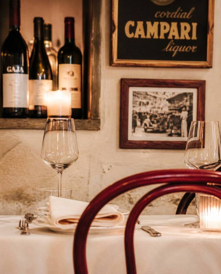 Tavolo apparecchiato in una trattoria italiana, luce di candela e sedia bordeaux